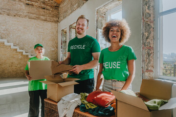 Happy activists standing with donation boxes and clothes in apartment