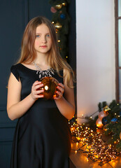 Cute girl in a black dress holding a golden ball. The interior design is dark with lights. Christmas. Make a wish. Holidays concept