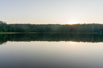 Fototapeta premium Lake surrounded by trees that reflect in the water. Fog on the surface of the forest