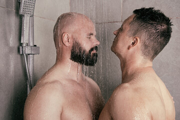 An attractive adult gay couple washes in the shower together. Love and relationship between two men. - obrazy, fototapety, plakaty