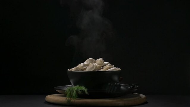 Hot dumplings in a black plate with smoke and dill on a dark background.