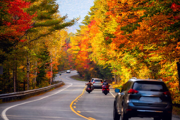 Cars and motorcycles moving along a steep narrow road among a bright colorful autumn forest. USA.