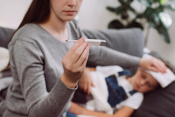 Selective focus of young mother treating sick daughter kid suffering from flu and fever, holding...