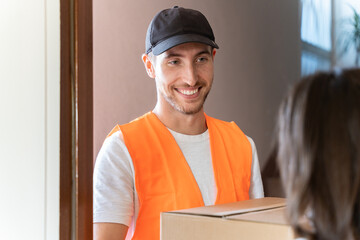 Delivery man delivers package to customer at home. Smiling carrier man dispatching a cardboard box.
