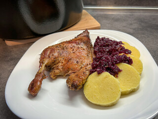 Roasted duck leg, red cabbage and potato dumpling on white plate