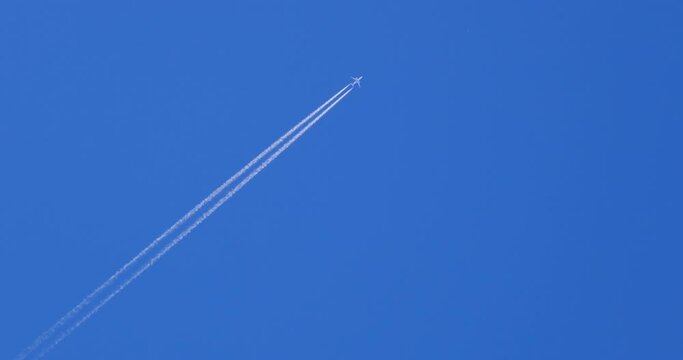 Airplane flying on deep blue sky with chemical direction trails, view from a distance