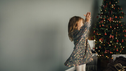 Blurred defocused image of cute girl wearing sparkling dress dancing in a decorated bedroom with a Christmas tree.