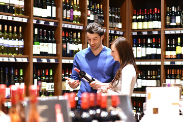 young couple in the supermarket shopping and choosing a bottle of wine