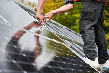Man mounter mounting photovoltaic solar panels on roof of house. Close up view of engineer...