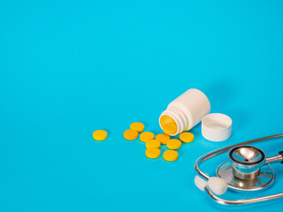 Modern acoustic stethoscope for doctor and yellow pills and plastic white bottle. Blue background with copy space for text