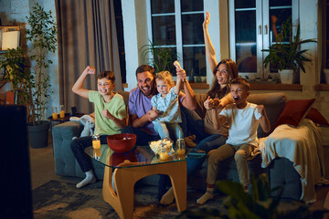 Family watching football match at home. Mother, father and children sitting on ouch at home and cheering up sport team. Concept of family, leisure time, relaxation, childhood and parenthood
