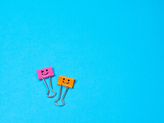 Funny smile metal binder clip or multicolored paperclip on blue background with copyspace for text