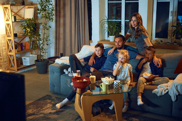 Happy loving family, parents and children sitting on couch in the evening at home and watching tv,...