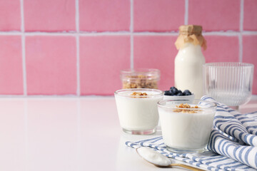 Bowls with yogurt and berries, bottle with milk and towel on pink background, space for text