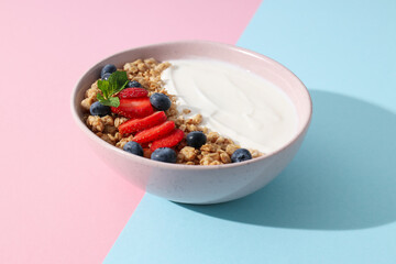 Bowl with yogurt and berries on pink and blue background