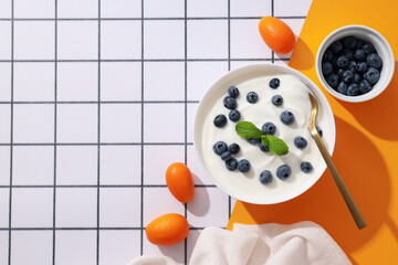 Bowls with yogurt and berries, spoon and towel on white and yellow background, space for text