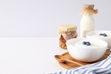 Bowls with yogurt, berries, bottle with milk and jars on white background, space for text