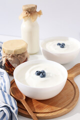 Bowls with yogurt, berries, bottle with milk and jars on white background