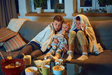Emotional children, boys and little girl sitting on couch at home and watching tv, horror movie....