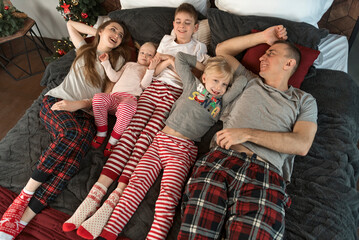 Fototapeta premium Happy young family wear pajamas and lie on large bed. Mother father and three children. Top view. Christmas or New Year Morning. Holidays