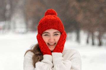 Happy young woman in red hat, mittens smile in snowy park. Portrait of brunette in nature in winter