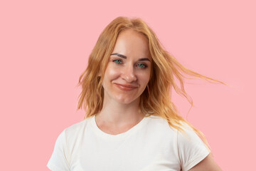 Portrait of smiling young woman with ginger wavy hair and green eyes looking in the camera. Beautiful confident woman. Pink background