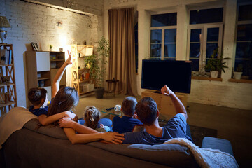 Back view. Family, parents and children sitting on couch in evening at home and watching football...