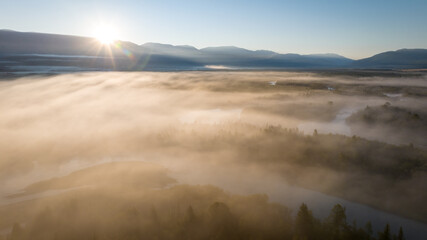 Early morning landscape. Foggy river. River valley in the morning fog at sunrise. View from above. Rays of the sun breaking through the fog in over the trees