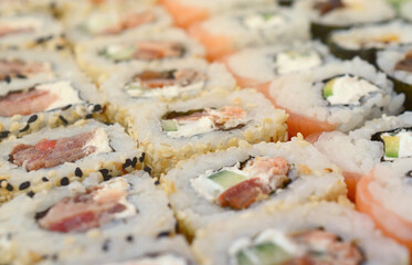 Close-up of a lot of sushi rolls with different fillings lie on a wooden surface. Macro shot of cooked classic Japanese food with a copy space.