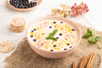 Yoghurt with bilberry and caramel in ceramic bowl on gray concrete, side view.