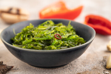 Chuka seaweed salad in blue ceramic bowl on brown concrete. Side view, selective focus