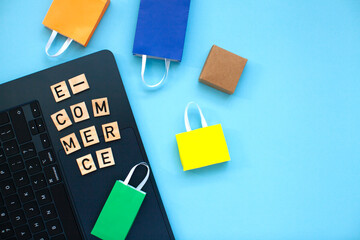 E-commerce and online shopping concept. Laptop, colourful bags and  wooden letters on the blue background. Top view.