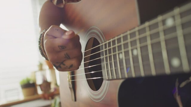 Close up of hands of unrecognizable woman using pick while playing acoustic guitar indoors