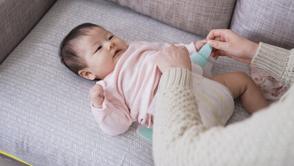 cropped shot mother’s hands fastening the fresh diaper for her lovely baby daughter who is lying...