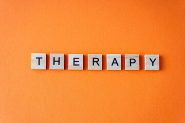 Word therapy. The phrase is laid out in wooden letters top view. Orange flat lay background....