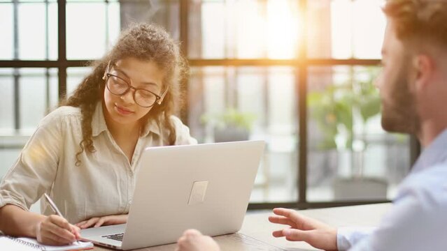 woman in glasses receives a client sitting at a laptop