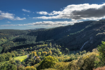 Fototapeta na wymiar Tall Powerscourt Waterfall, valley, forests in autumn colours illuminated by sunlight. Scenic Wicklow Mountains, Ireland
