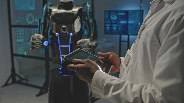 Cropped shot of unrecognizable electronics engineer controlling human robot via use of digital tablet in dark lab