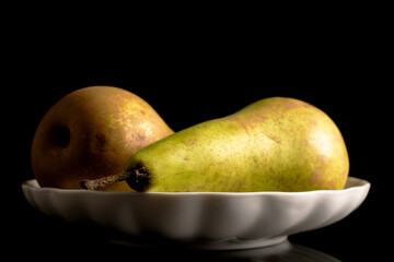 Two ripe pears on a white ceramic plate, macro, isolated on black background.