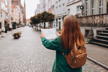 Portrait redhead woman with paper map on urban street. Happy tourist travels in Europe. Vacation...