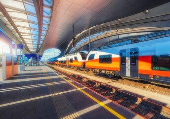 High speed train on the modern railway station at sunset in Graz, Austria. Beautiful orange intercity passenger train on the covered railway platform. Railroad. Passenger railway transportation