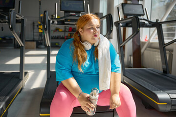 Tired plus size woman with towel feeling exhaustion after training