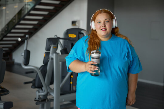 Portrait of young overweight woman wearing sportive clothes and headphones at gym