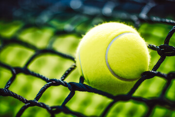 Close up shot of beautiful new tennis ball hitting a net in the middle of a match, brand new tennis ball in net with tennis court in the background
