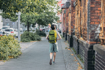 View back from the teenage girl with green backpack on the way to school - obrazy, fototapety, plakaty