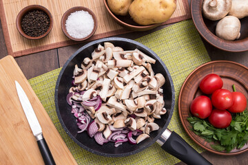 Cooking healthy vegan vegetarian food concept. Frying pan with sliced mushrooms and onion. Vegetables on kithchen table. Top view, flatlay