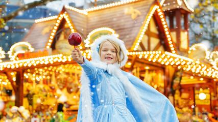 Little girl as snow white with candy sweet caramel apple from a sweets stand on Christmas market.