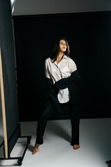 Stylish girl posing in a black suit and white shirt in a professional photo studio. Fashion shooting concept