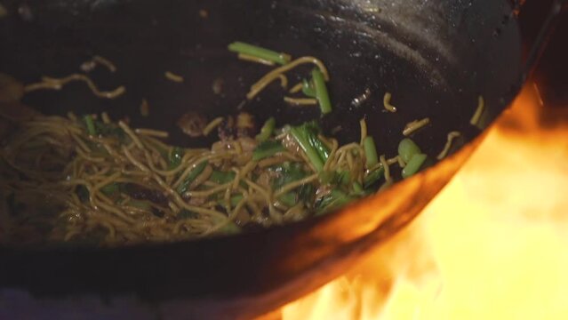 The chef is frying Hokkien noodles in a pan over a hot fire and steam, a local Phuket food.