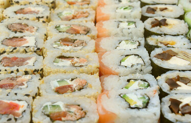 Close-up of a lot of sushi rolls with different fillings lie on a wooden surface. Macro shot of cooked classic Japanese food with a copy space.